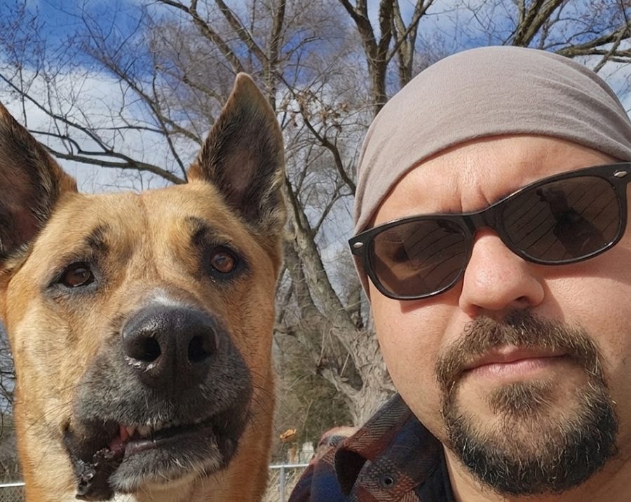 Chad Perera outdoors with a tan shepherd mix, both looking at the camera